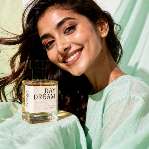 Woman holding a 'Day Dream' perfume bottle with a light green background